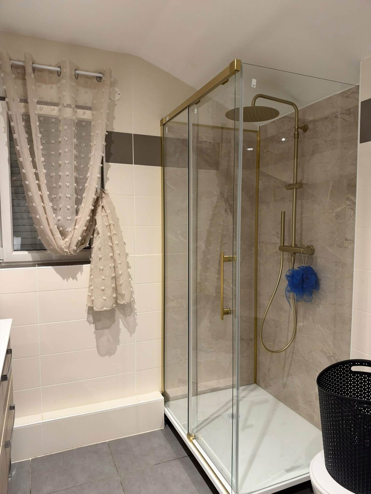 Douche rénovée avec parois vitrées, finitions dorées et revêtement mural effet marbre